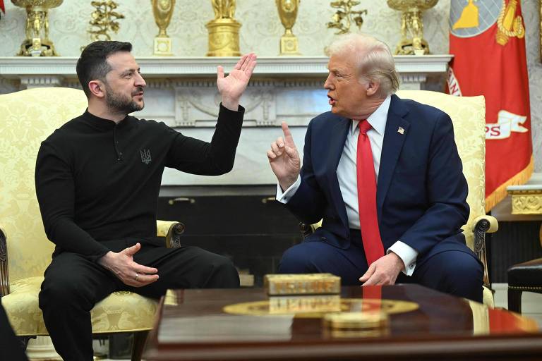 A imagem mostra dois homens sentados em cadeiras em um ambiente formal. À esquerda， um homem com cabelo curto e barba， vestindo uma camisa preta， gesticula com a mão. À direita， um homem com cabelo loiro e uma gravata vermelha， que parece estar falando. Ao fundo， há uma decoração elaborada com elementos dourados e bandeiras.