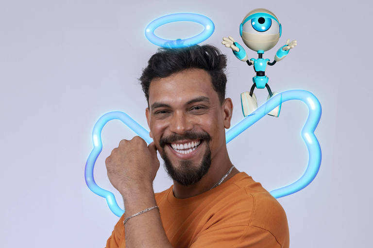 Um homem sorridente está posando com o braço dobrado e a mão no queixo. Ele usa uma camiseta laranja e tem cabelo curto e escuro. Atrás dele, há um fundo claro com um desenho de nuvem azul e um personagem animado com um olho grande e um halo acima da cabeça, que parece estar flutuando.
