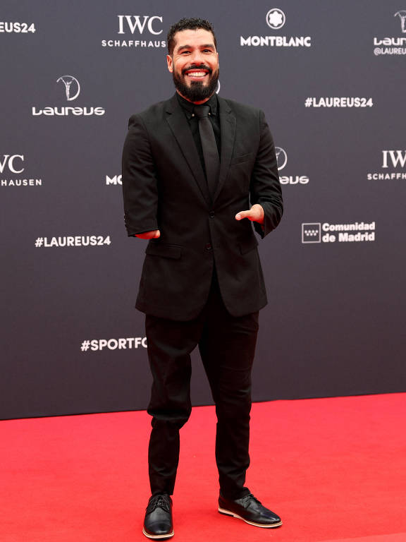 Um homem sorridente， que é o brasileiro Daniel Dias， está posando em um tapete vermelho durante um evento de premiação. Ele usa um terno preto e uma gravata， com sapatos pretos. O fundo apresenta logotipos de patrocinadores e o nome 039;Laureus 24039;.