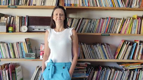 Cristina Pizarro diante de estante de sua Casa Sebo da Cris, em Itajubá (MG)