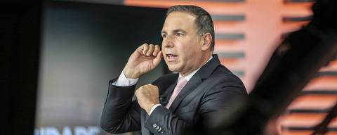 EXCLUSIVO F5 - Reinaldo Gottino posa para o F5 durante comando do Cidade Alerta, da Record *** Local Caption *** Um apresentador de televisão está em um estúdio, gesticulando com as mãos enquanto fala. Ele usa um terno escuro e uma gravata rosa. Ao fundo, é possível ver o nome do programa 'CIDADE ALERTA' em letras grandes. O ambiente é bem iluminado, com um design moderno.