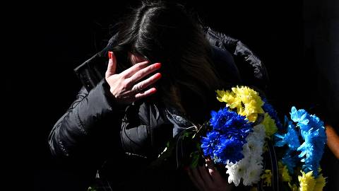 A woman holds a bunch of flowers in the colours of the Ukrainian flag, as she walks to attend the funeral of a Ukrainian serviceman in the western Ukrainian city of Lviv on March 19, 2025, amid the Russian invasion of Ukraine. (Photo by YURIY DYACHYSHYN / AFP)