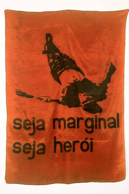 A imagem apresenta um pôster com fundo laranja e uma figura em preto de uma pessoa deitada, aparentemente em uma posição de queda. Abaixo da figura, há um texto em letras grandes que diz: 'seja marginal seja herói'.
