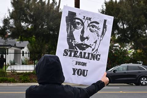 (FILES) A person holds a sign with a drawing of Elon Musk while protesting outside a Tesla dealership in Los Angeles, California on March 14, 2025. US President Donald Trump suggested on March 21, 2025, that people who vandalize Tesla property, the car brand owned by his billionaire ally Elon Musk, could be deported to prisons in El Salvador. (Photo by Frederic J. BROWN / AFP)