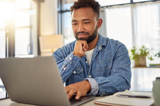 Happy businessman working on his laptop at home. Handsome businessman reading an email on his laptop at home. Freelance entrepreneur typing on his laptop at home. Virtual remote worker at home