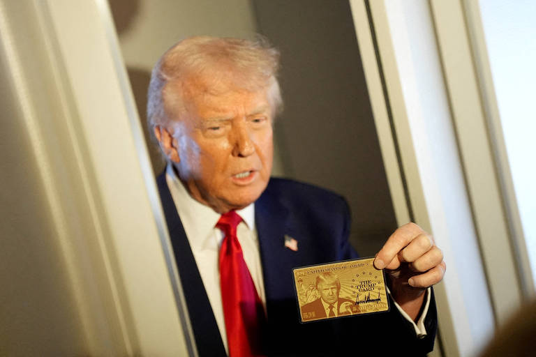 Trump, um homem com cabelo loiro e terno escuro, está segurando um cartão dourado. Ele parece estar em uma porta, com uma expressão de seriedade. O fundo é desfocado, mas parece ser um ambiente interno.