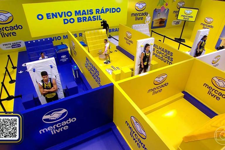 A imagem mostra um espaço de marketing do Mercado Livre, decorado em amarelo e azul. Há várias áreas delimitadas, com pessoas interagindo em diferentes seções. O fundo exibe o slogan 'O ENVIO MAIS RÁPIDO DO BRASIL' e há um código QR no canto inferior esquerdo. O ambiente parece ser uma instalação promocional, com elementos visuais que destacam a marca.
