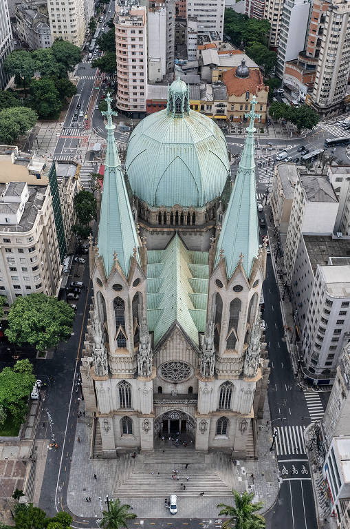 Imagem aérea mostra a Catedral da Sé, no Centro de São Paulo. Trata-se de uma igreja de grandes proporções projetada em estilo neogótico. Tem duas torres de 92m na fachada, com telhados pontiagudos. Possui também grandes vitrais desenhados.