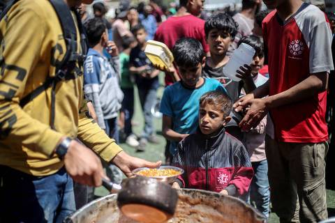 Palestinians wait in front of a free food distribution point to receive their portion of a hot meal, at the Nuseirat refugee camp in the central Gaza Strip on April 19, 2025. (Photo by Eyad BABA / AFP)