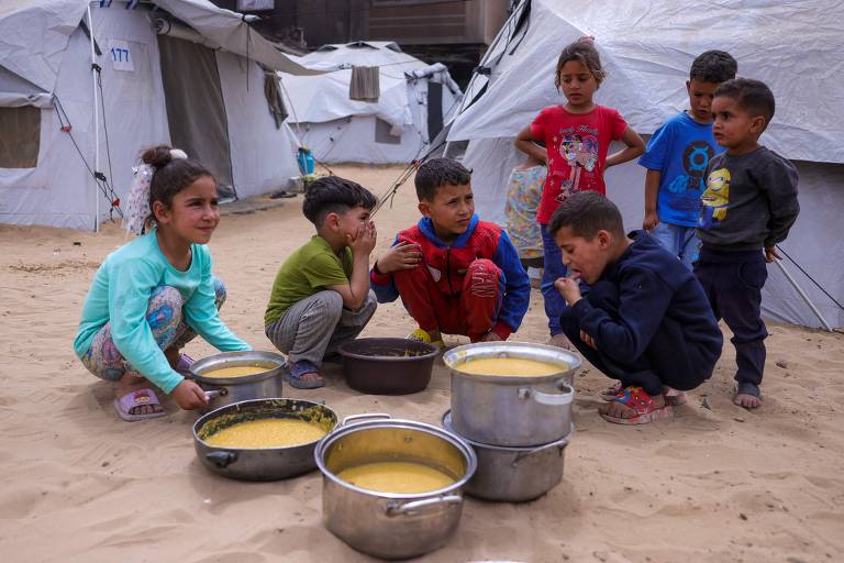 Crianças diante de panelas com comida em campo de deslocados em Gaza