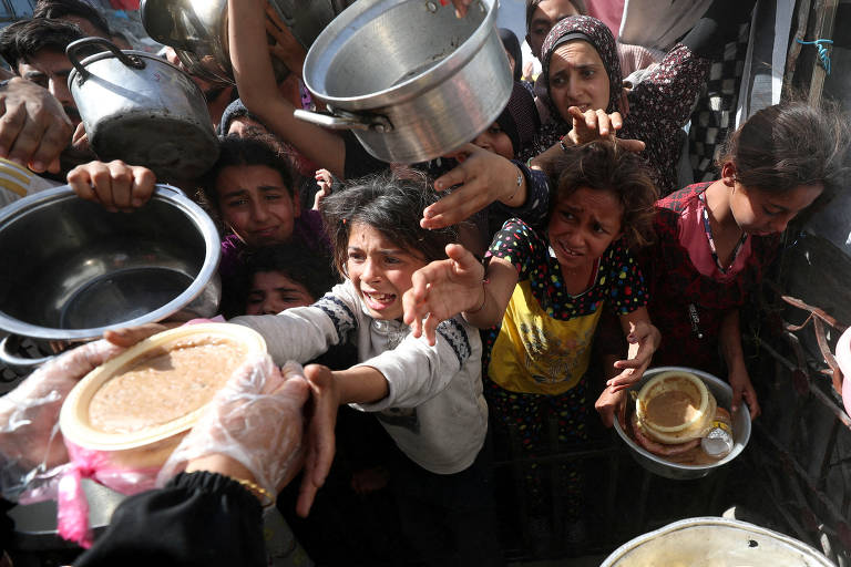 Crianças e adultos se aglomeram e disputam prato de comida em Gaza