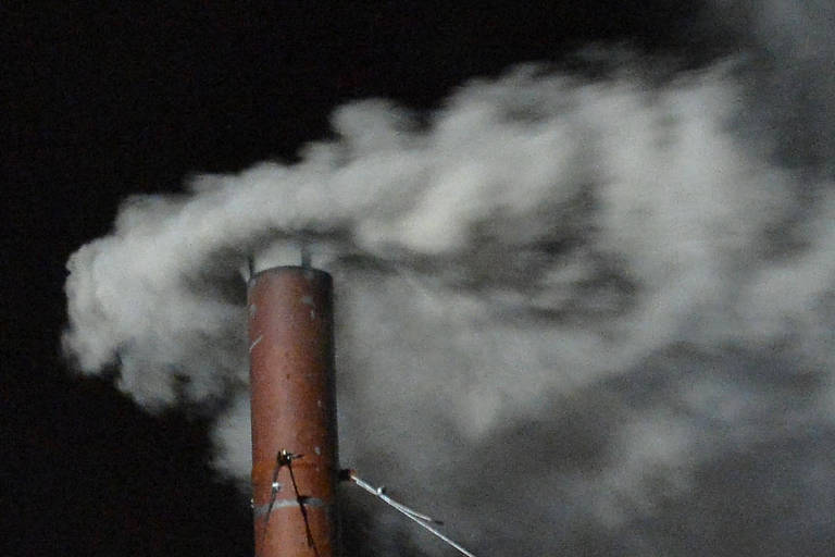 A imagem mostra uma chaminé de metal, de cor marrom, emitindo uma densa coluna de fumaça branca. O fundo é escuro, sugerindo que a foto foi tirada à noite. A fumaça se dispersa no ar, criando um efeito visual de movimento.