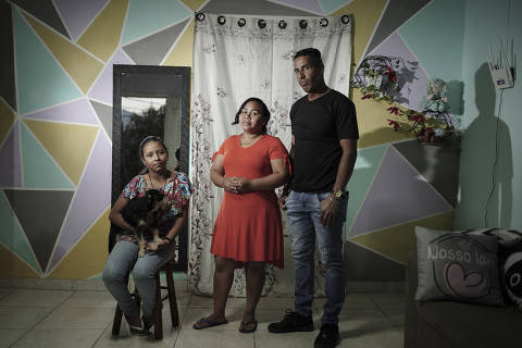 PORTO ALEGRE, RS - 15/04/2025 - Tragédia climática no RS completa 1 ano e recriamos algumas fotos feitas no ano passado. Os venezuelanos Javier Baez Velázquez, a esposa Carina Baez, a filha Berenice Baez e a cachorra Violeta, moravam no bairro Sarandi e foram afetados em maio de 2024, tendo que viver por meses em abrigos.  A reportagem sobre o assunto foi publicada no jornal Folha de S.Paulo. Hoje, a família voltou a morar no mesmo bairro, dessa vez numa casa com andar alto. Na foto, eles na nova residência com poucos móveis.  (FOTO: Carlos Macedo/Folhapress). ***Exclusivo Folha de S.Paulo*** ORG XMIT: Fotógrafo
