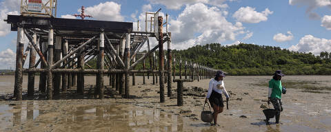 ILHA DE MARÉ, BA, BRASIL 06/03/2025 - Verônica Faria,39, e Luciana Paraguassu,25,  caminhando próximo a uma antiga estrutura deixada pela refinaria de petróleo Landulpho Alves-Mataripe. A região da ilha sofre com a contaminação por metais pesados.Série Excluídos do Clima. (Foto: Rafaela Araújo/Folhapress, AMBIENTE) *** EXCLUSIVO FOLHA***