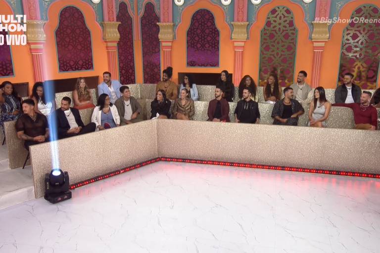 A imagem mostra um grupo de pessoas sentadas em um estúdio de televisão. O ambiente é decorado com elementos coloridos e arcos, criando uma atmosfera vibrante. As pessoas estão dispostas em um formato de U, com algumas olhando para a câmera e outras conversando entre si. No canto superior esquerdo, há um logotipo que diz 'MULTISHOW AO VIVO'.