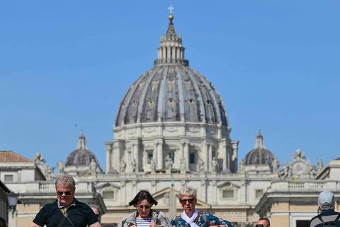 Pedestrians walk on Via della Conciliazione in Rome, with a view of the Vatican's St Peter Basilica after the transfer of the coffin of Pope Francis from the chapel of Santa Marta to St Peter's Basilica, following the Pope's death, on April 23, 2025. Pope Francis's body arrived at Saint Peter's Basilica on Apri; 23, 2025, to lie in state before his weekend funeral. The late pope's open wooden coffin was carried by pallbearers the 500 metres (yards) from the Casa Santa Marta where he lived and died, behind a procession of red-robed cardinals. (Photo by Andrej ISAKOVIC / AFP)