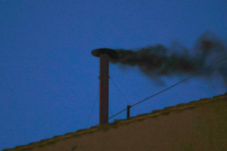 A imagem mostra uma chaminé de metal em um telhado, emitindo fumaça preta contra um céu azul escuro. A chaminé é vertical e possui uma tampa na parte superior. Há um fio preso à chaminé, e a fumaça se dispersa no ar.
