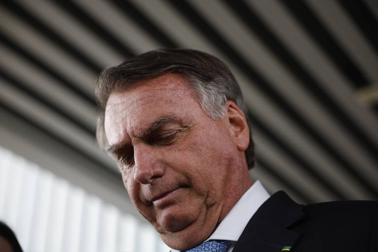 Um homem com cabelo grisalho e uma expressão pensativa, olhando para baixo. Ele está vestido com um terno escuro e uma gravata clara. O fundo apresenta linhas verticais, sugerindo um ambiente interno com iluminação suave.