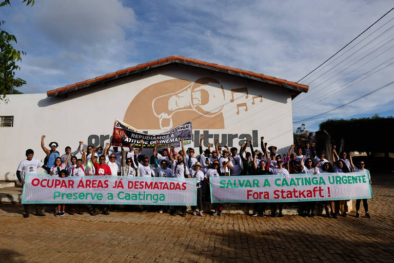 A imagem mostra um grupo de pessoas reunidas em frente a um edifício com o logotipo de uma organização cultural. Elas seguram faixas com mensagens de protesto, como "OCUPAR ÁREAS JÁ DESMATADAS" e "SALVAR A CAATINGA URGENTE". O ambiente é ao ar livre, com céu parcialmente nublado e vegetação ao redor.