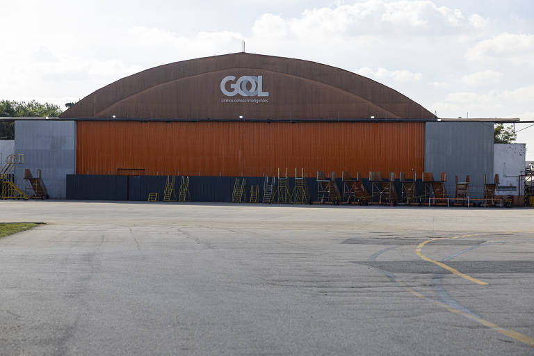 Hangar com teto arredondado e portão laranja fechado. No alto está escrito Gol