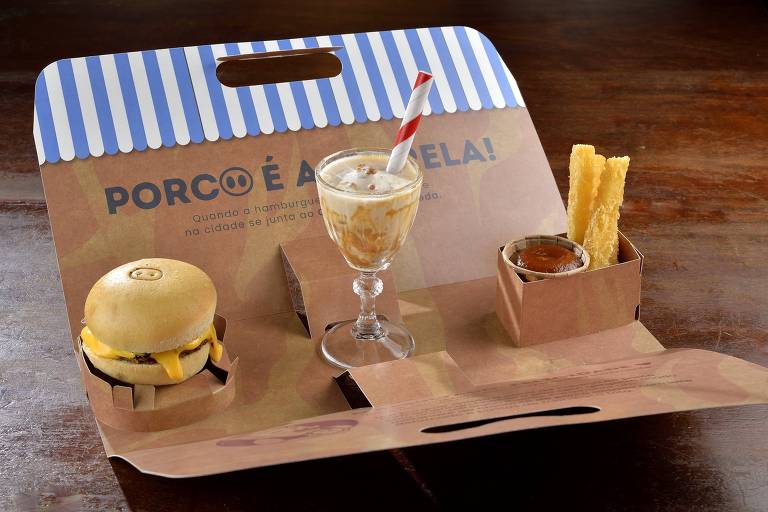 A imagem mostra uma bandeja de papel com um hambúrguer, um copo de sobremesa com canudo, e palitos de churros. O hambúrguer é pequeno e tem queijo visível. O copo de sobremesa contém um creme e um canudo listrado. Ao lado, há uma porção de churros com um pequeno recipiente de molho.