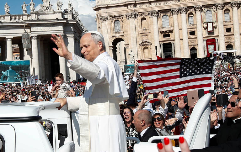 Uma bandeira dos EUA é levantada enquanto o Papa Leão 14 acena para os fiéis do papamóvel antes de sua missa de início do pontificado na Praça de São Pedro
