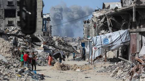 TOPSHOT - Smoke billows to the north as Palestinians move with their belogings through Jabalia while fleeing the northern Gaza Strip towards Gaza City on May 19, 2025, amid Israeli evacuation orders and ongoing strikes. Israel said on May 19 it will 