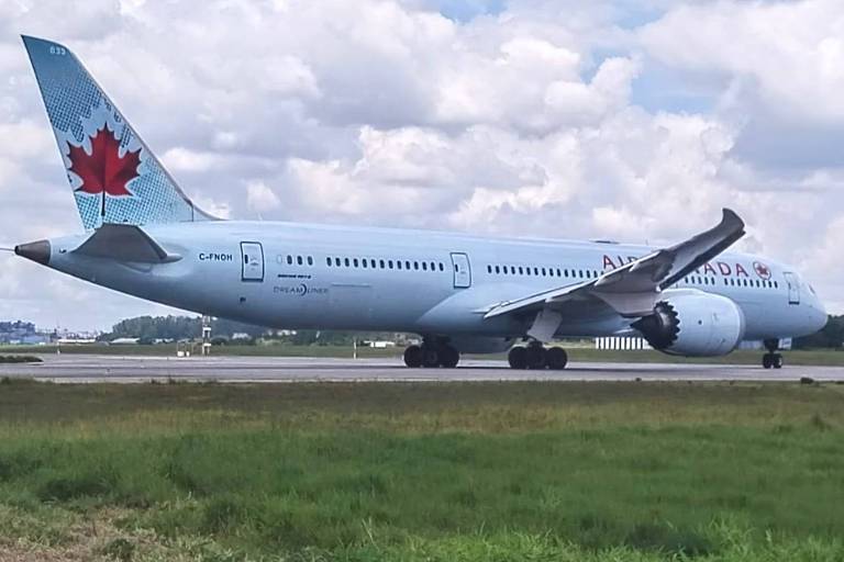 Een Boeing 787 van Air Canada taxiet op een landingsbaan. Het vliegtuig is lichtblauw met rode accenten, waaronder een esdoornblad op de staart. De lucht is gedeeltelijk bewolkt en er is een groen vlak op de voorgrond.