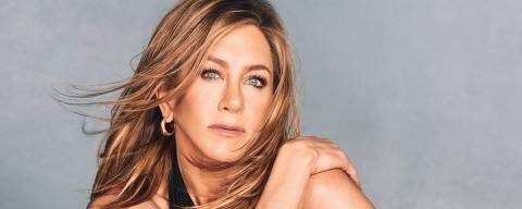 Jennifer Aniston contou em 2018 que uma assombração morava em sua casa e mexia nas coisas. 'A máquina de lavar louça começava a funcionar, a cafeteira começava a funcionar ou o aparelho de som ligava no volume máximo' *** Local Caption *** A imagem mostra uma mulher sentada em uma superfície escura, com um fundo cinza. Ela está usando um traje preto e meias-calças, com faixas pretas em torno de seus tornozelos. A mulher tem cabelo longo e solto, e está olhando diretamente para a câmera com uma expressão séria. Sua pose é elegante, com um braço envolvendo uma perna e o outro apoiado no ombro.