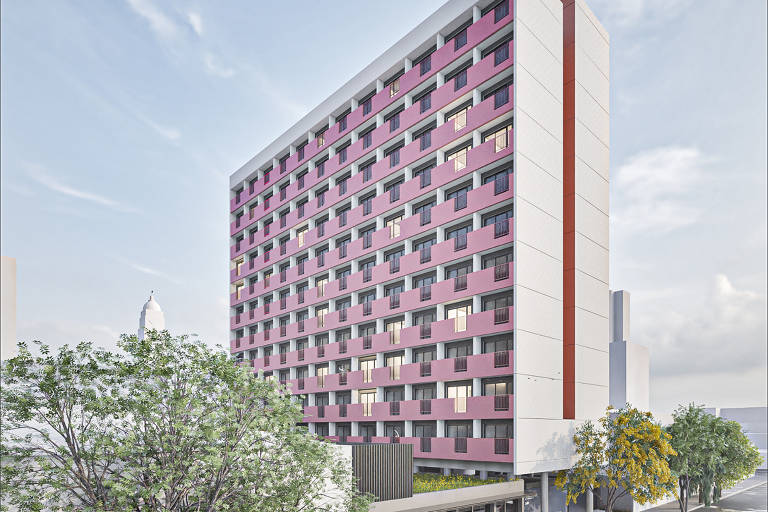 A imagem mostra um edifício moderno de vários andares, com uma fachada predominantemente rosa e janelas em diferentes tamanhos. O prédio é cercado por árvores e há uma calçada na frente, onde se pode ver uma área comercial no térreo. O céu está claro, sugerindo um dia ensolarado.