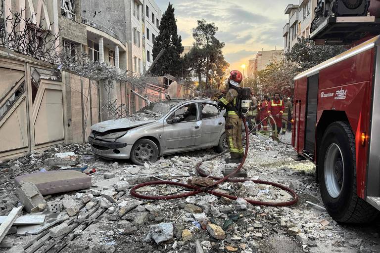 A imagem mostra um cenário de desastre, com um carro danificado em meio a escombros. Bombeiros estão presentes, um deles está usando equipamento de proteção e segurando uma mangueira. Ao fundo, há prédios danificados e uma luz do sol poente. O ambiente é caótico, com detritos espalhados pelo chão.