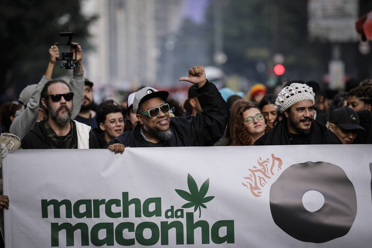 Integrantes da banda Planet Hemp —Rafael Crespo, BNegão e Marcelo D2, da esq. à dir.— seguram faixa da Marcha da Maconha na avenida Paulista, que traz o lema 'O Clima Tá Tenso! Reparação, Direitos e Liberdade'