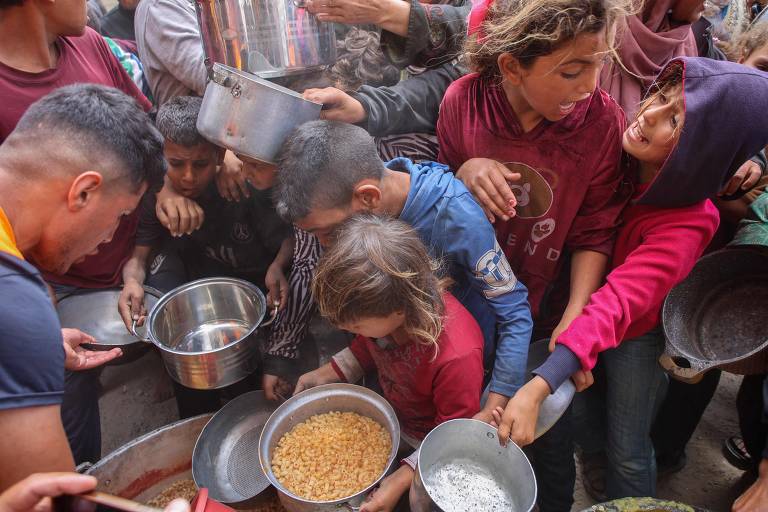 Palestinos se empurram para receber ração de comida quente em cozinha beneficente no campus de universidade na Cidade de Gaza