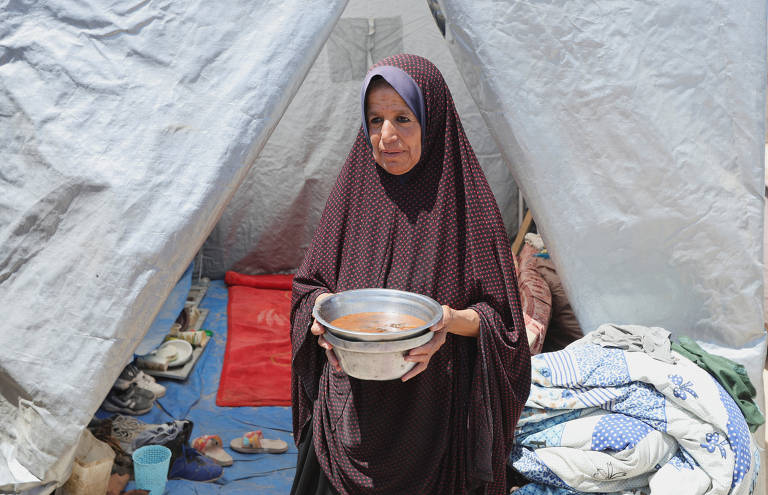 Basma Al-Sheikh Khalil, palestina, segura tigela metálica de comida em frente à barraca onde se abrigou após ser deslocada