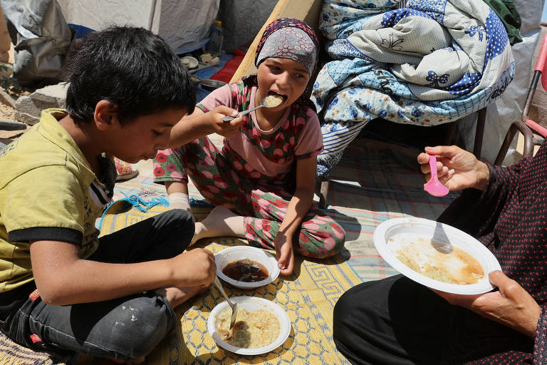 Basma Al-Sheikh Khalil, palestina, come com seus netos em frente à barraca onde se abrigaram após serem deslocados