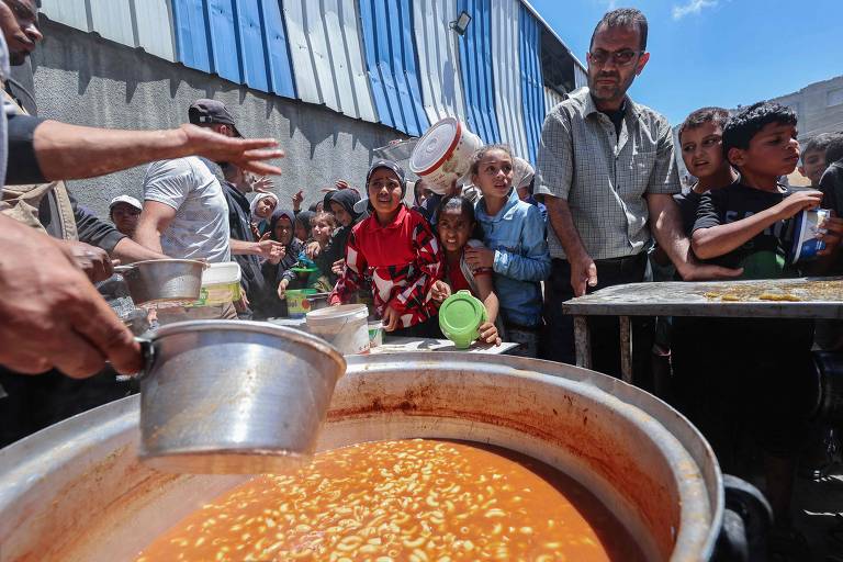Palestinos fazem fila para receber refeição quente do Programa Mundial de Alimentos, da ONU, no campo de refugiados de Nuseirat