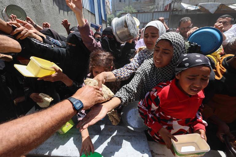 Palestinos erguem os braços para tentar conseguir alimento no campo de refugiados de Nuseirat