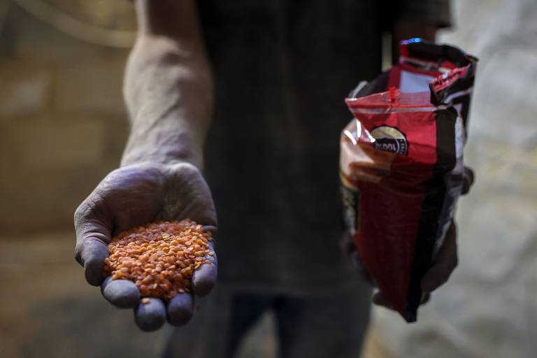 Palestino exibe lentilhas secas e macarrão enquanto se prepara para moê-los em farinha para fazer pão durante no campo de refugiados de Jabalia