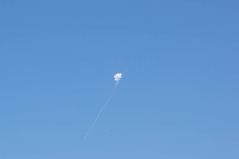 A imagem mostra um céu azul claro com uma nuvem branca visível no centro, que parece ser a fumaça de um foguete em ascensão. Há uma trilha deixada para trás, indicando o caminho do foguete.