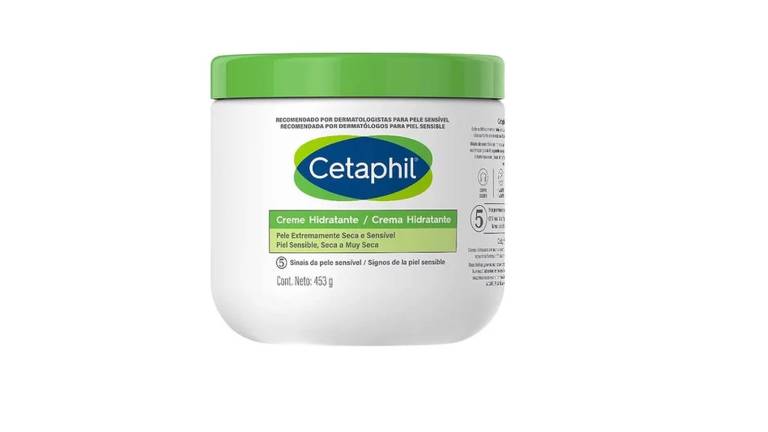 A imagem mostra um pote de creme hidratante da marca Cetaphil. O pote é branco com uma tampa verde. Na frente, há o logotipo da marca e a descrição do produto em português, indicando que é um creme hidratante para pele seca e sensível. O peso do produto é de 453 gramas.