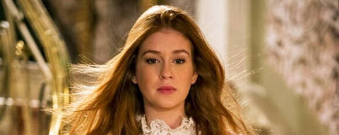 Marina Ruy Barbosa em 'Amor à Vida' (2014) *** Local Caption *** Uma jovem mulher está descendo uma escada em um ambiente elegante. Ela usa um vestido de noiva branco, com detalhes em renda e mangas longas. O vestido tem um corpete com um design floral e uma saia volumosa. Seu cabelo é longo e solto, e ela tem uma expressão séria. Ao fundo, pode-se ver uma escada de metal dourado e uma parede decorada.
