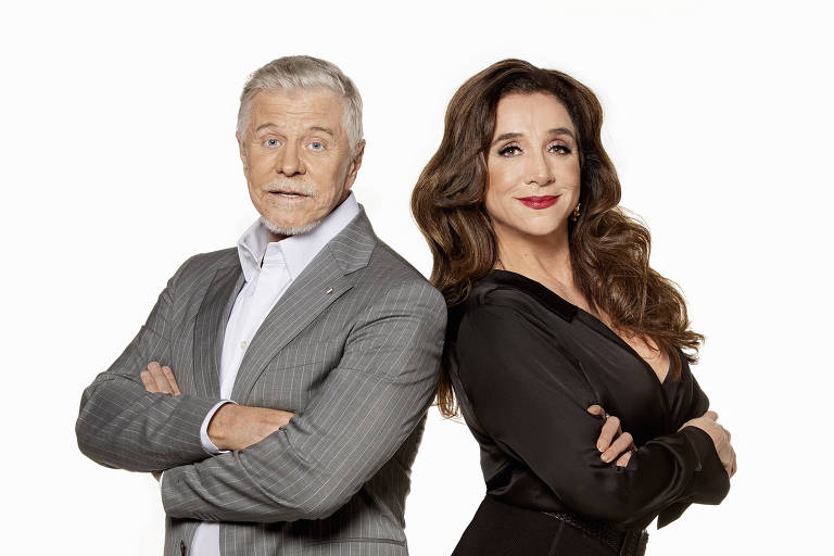 A imagem mostra dois personagens em pé, um ao lado do outro, com os braços cruzados. À esquerda, um homem idoso com cabelo grisalho, vestindo um terno cinza listrado e uma camisa branca. À direita, uma mulher com cabelo longo e ondulado, vestindo um vestido preto justo. Ambos estão olhando para frente, com expressões confiantes, e o fundo é branco.