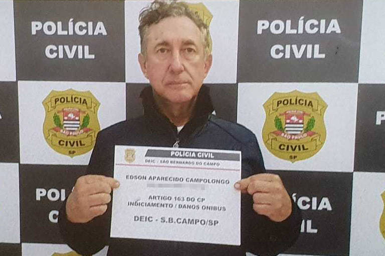 De afbeelding toont een man van middelbare leeftijd met grijs haar die poseert voor een arrestatiefoto. Hij houdt een bord vast met informatie over zijn arrestatie. De achtergrond van de afbeelding bestaat uit borden van de Civil Police, met het politielogo en de tekst 'POLÍCIA CIVIL' in een patroon herhaald. De man draagt een donker jasje en heeft een neutrale uitdrukking.