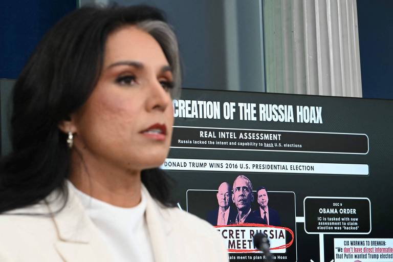 A imagem mostra uma mulher com cabelo escuro e liso, vestindo uma blusa branca, em primeiro plano. Ao fundo, há uma tela com texto que diz "CREATION OF THE RUSSIA HOAX" e "REAL INTEL ASSESSMENT", além de informações sobre a eleição presidencial dos EUA de 2016 e uma referência a uma ordem de Obama. O texto também menciona "SECRET RUSSIA MEET" com uma parte sublinhada em vermelho.