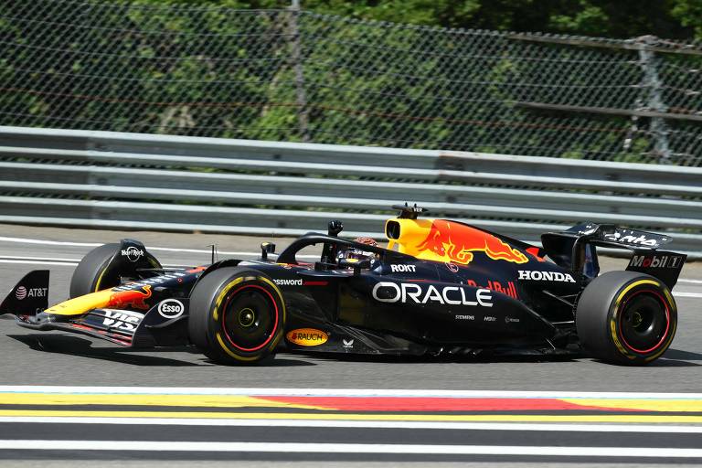 Um carro de Fórmula 1 da equipe Red Bull Racing, com a pintura predominante em preto e detalhes em vermelho e amarelo, está em movimento em uma pista. O carro possui pneus slick e está em uma curva, com a grade frontal visível e o logotipo da Honda. Ao fundo, há uma cerca de proteção e uma vegetação ao redor da pista.