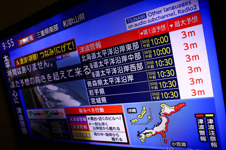 A imagem mostra uma tela de televisão exibindo informações sobre um alerta de tsunami. O fundo é azul e contém texto em japonês, incluindo horários e alturas de ondas esperadas em diferentes regiões do Japão. Há também um mapa do Japão com algumas áreas destacadas. O horário na parte superior da tela é 9:55.