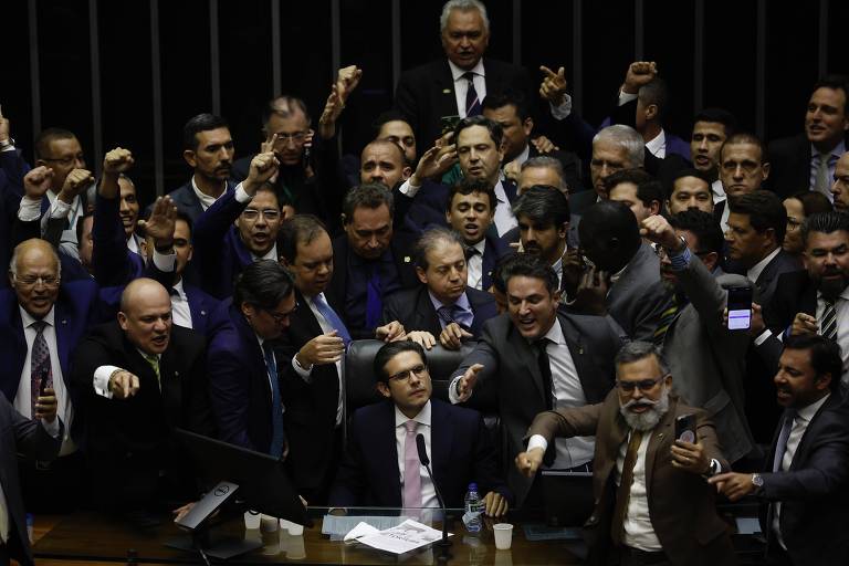 L'immagine mostra un gruppo di parlamentari in una sessione del Congresso Nazionale. Sono in piedi, con espressioni intense, alcuni alzano i pugni e altri gesticolano. L'ambiente è formale, con tavoli e apparecchiature per il voto sullo sfondo. La maggior parte degli uomini è in giacca e cravatta, e tra i presenti si respira un'atmosfera di eccitazione e di acceso dibattito.