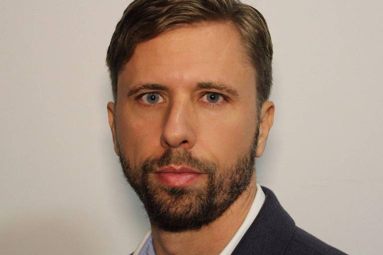 Een man met kort haar en een baard kijkt recht in de camera. Hij draagt een donker colbert en een licht overhemd. De achtergrond is neutraal en licht, waardoor zijn gezicht goed zichtbaar is.