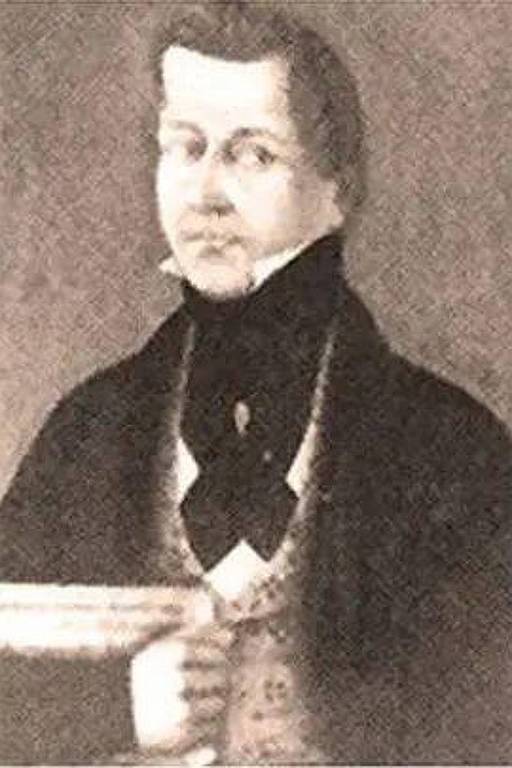 A imagem mostra um retrato em preto e branco de um homem do século XIX. Ele está vestido com um paletó escuro e uma gravata preta, com uma camisa clara visível. O homem tem cabelo claro e usa um colarinho alto. Ele segura um objeto em sua mão esquerda, mas não está claro o que é.