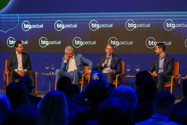 A imagem mostra um painel de discussão no AgroForum, com cinco homens sentados em cadeiras em um palco. Eles estão vestidos de forma formal e há um público visível na parte inferior da imagem. O fundo é azul com o nome 'AgroForum' e o logotipo da BTG Pactual. O ambiente parece ser um evento de conferência.